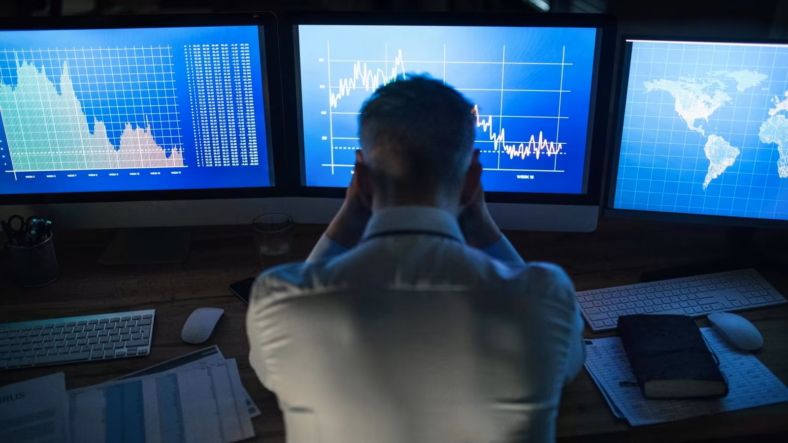 A trader sits in front of multiple screens holding his head. (Unsplash+/Getty Images)